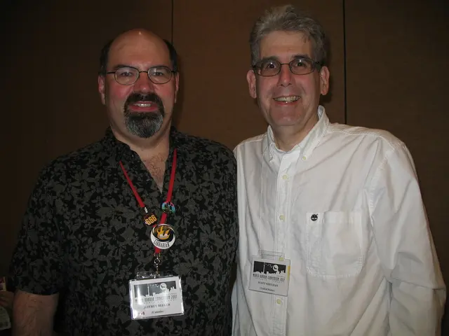 In this image we can see two men, they are wearing access cards with text on them, behind them we...