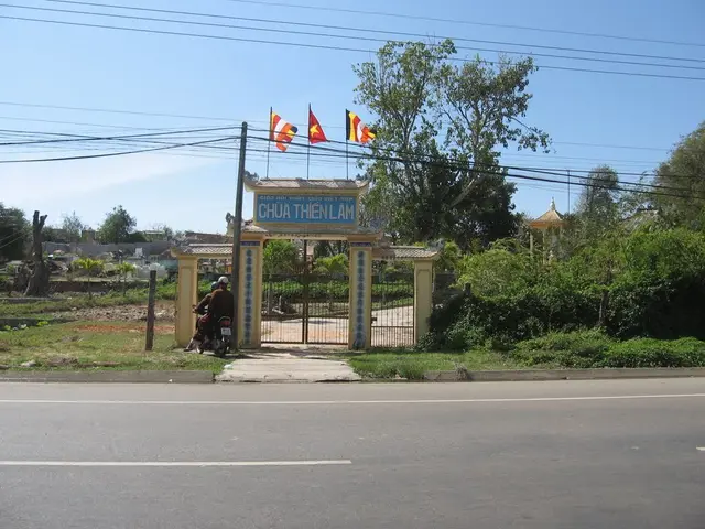 In this image, we can see an arch contains flags. There are some trees and plants on the right side...