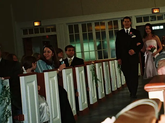 There are group of people sitting on the bench. And there is a bride and groom coming over. Bride...